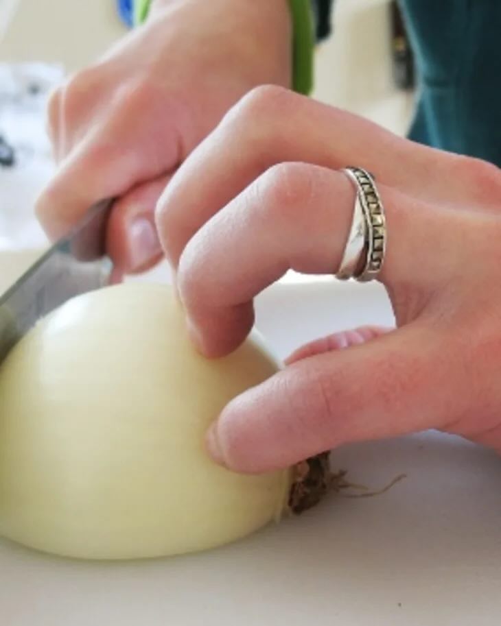 Man's hand holding a knife with a claw grip to slice an onion - photo credit Emma Christensen, TheKitchn.com